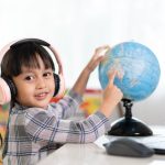 Asian beautiful little student girl is pointing on bilingual globe model for online lesson.