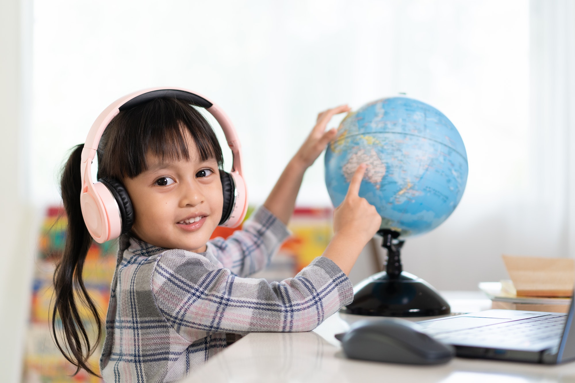 Asian beautiful little student girl is pointing on bilingual globe model for online lesson.